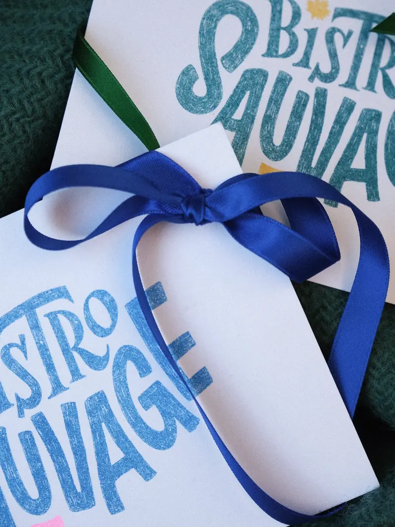 Le bon cadeau du Bistro Sauvage, carte imprimée en bleu et nouée d’un ruban.