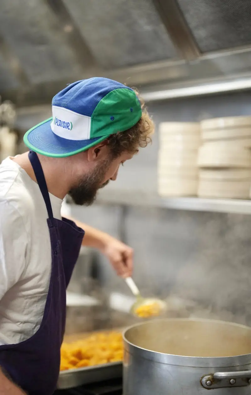 Un cuisinier en casquette (Plaisir) bleue et verte, devant les fourneaux.