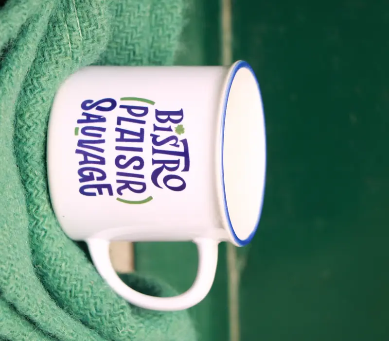 Le mug en céramique « Bistro (Plaisir) Sauvage » posé sur un pull vert.