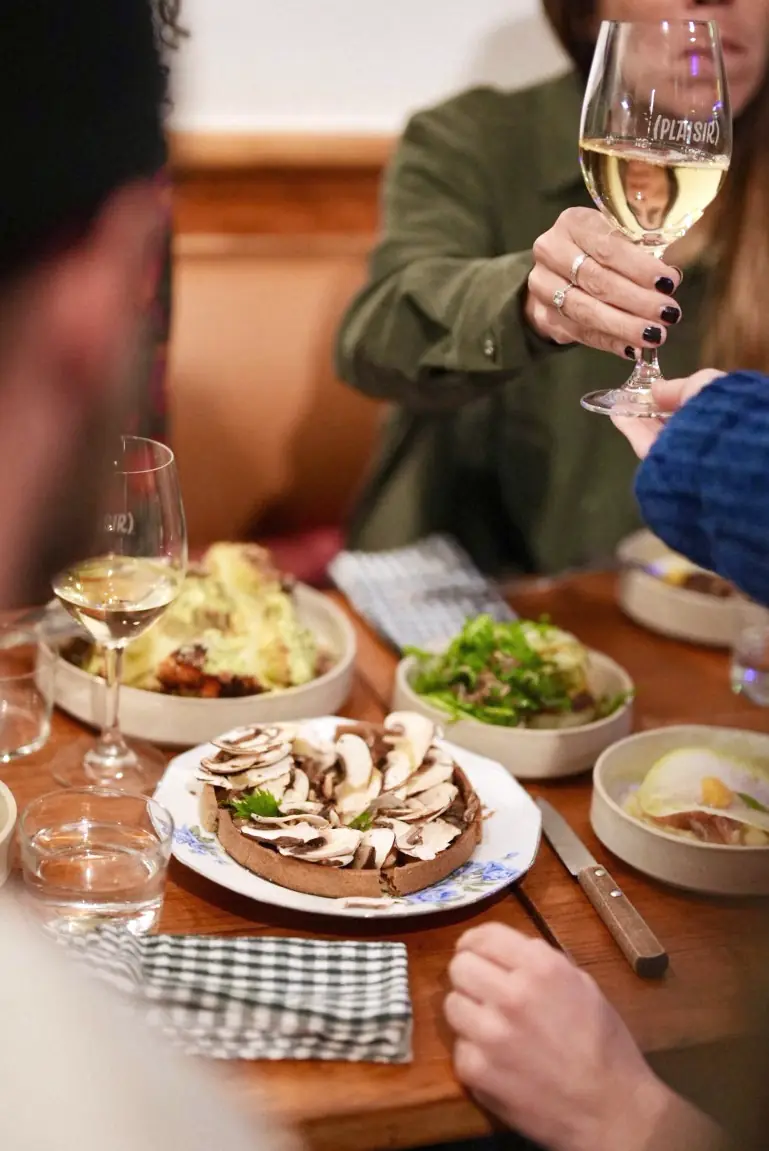 Une table du Bistro Sauvage : un verre de blanc levé, des assiettes à partager, une serviette à carreaux.