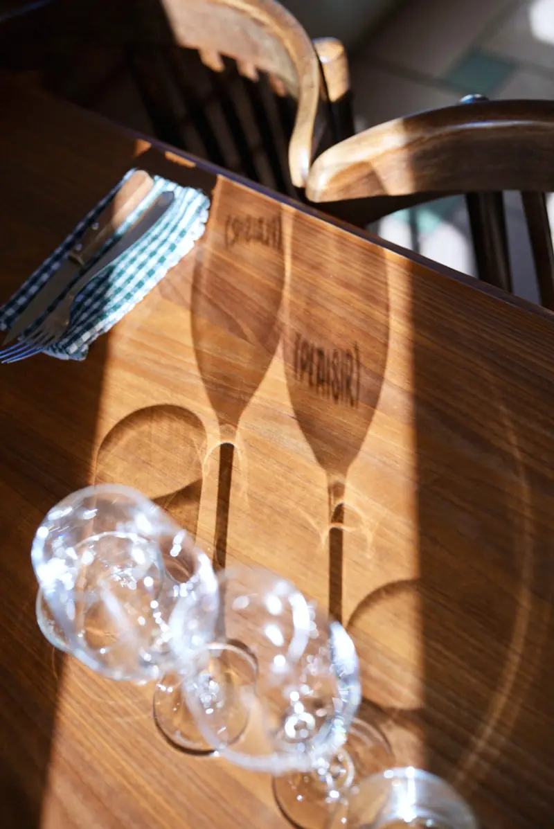 Deux verres à vin gravés (Plaisir) et leur ombre sur une table en bois, au soleil.